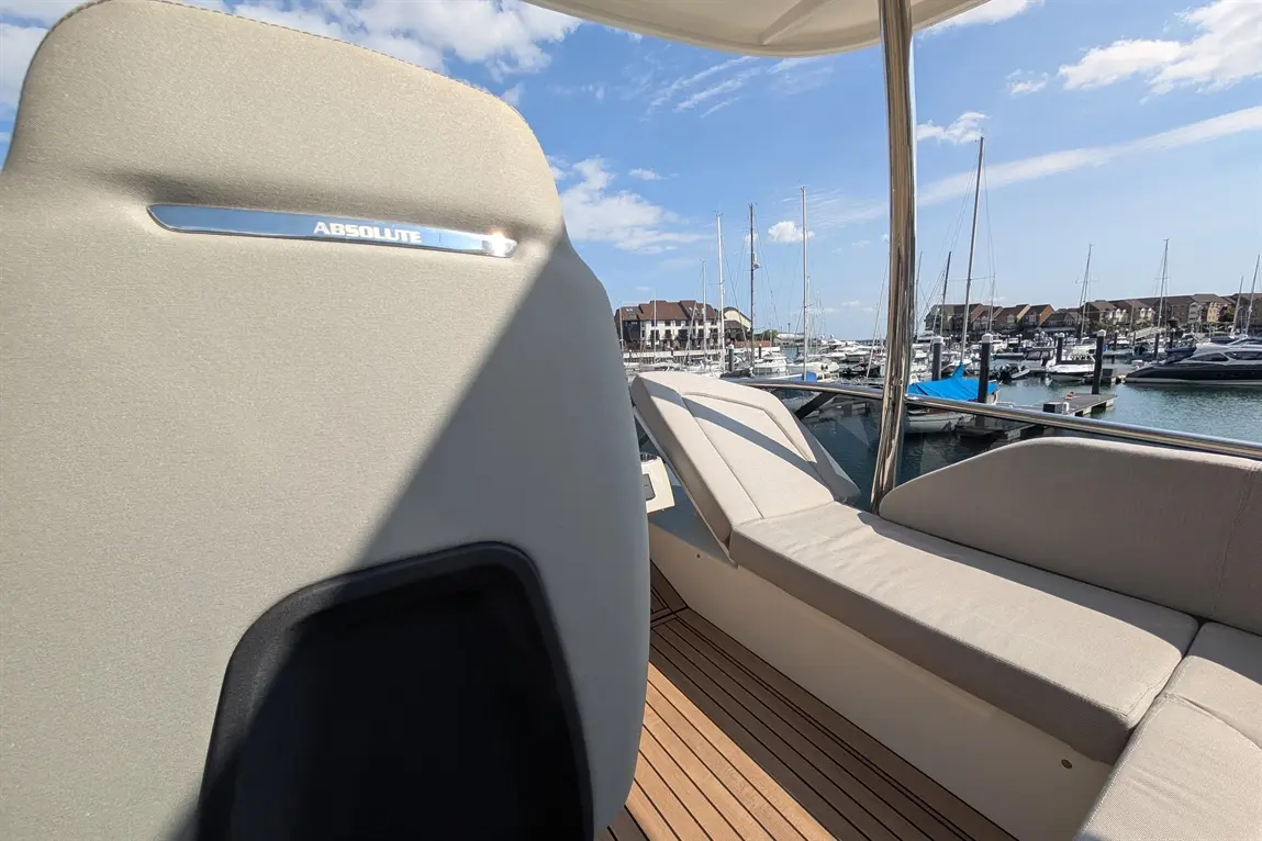 View from a boat featuring "ABSOLUTE" labelled seat, sun loungers, and a marina with yachts under a clear blue sky.